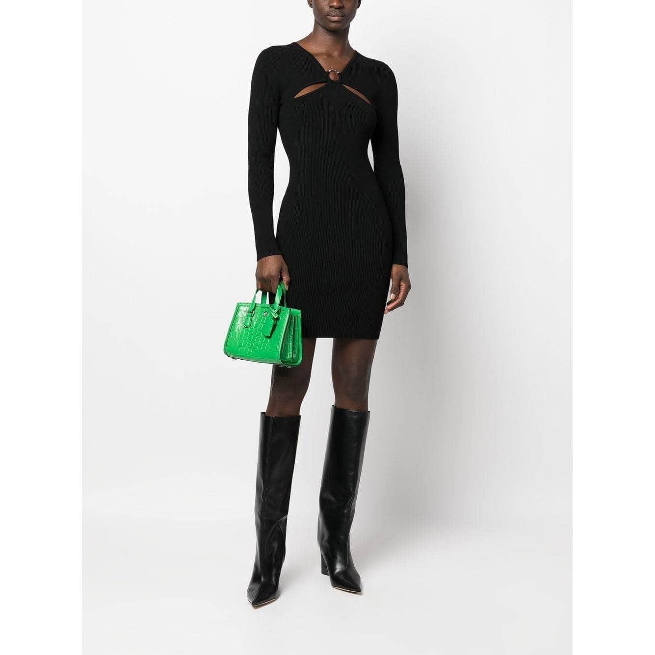 Model wearing MMK Dresses Black ribbed-knit mini dress with long sleeves and cut-out detailing, paired with knee-high boots and green handbag.