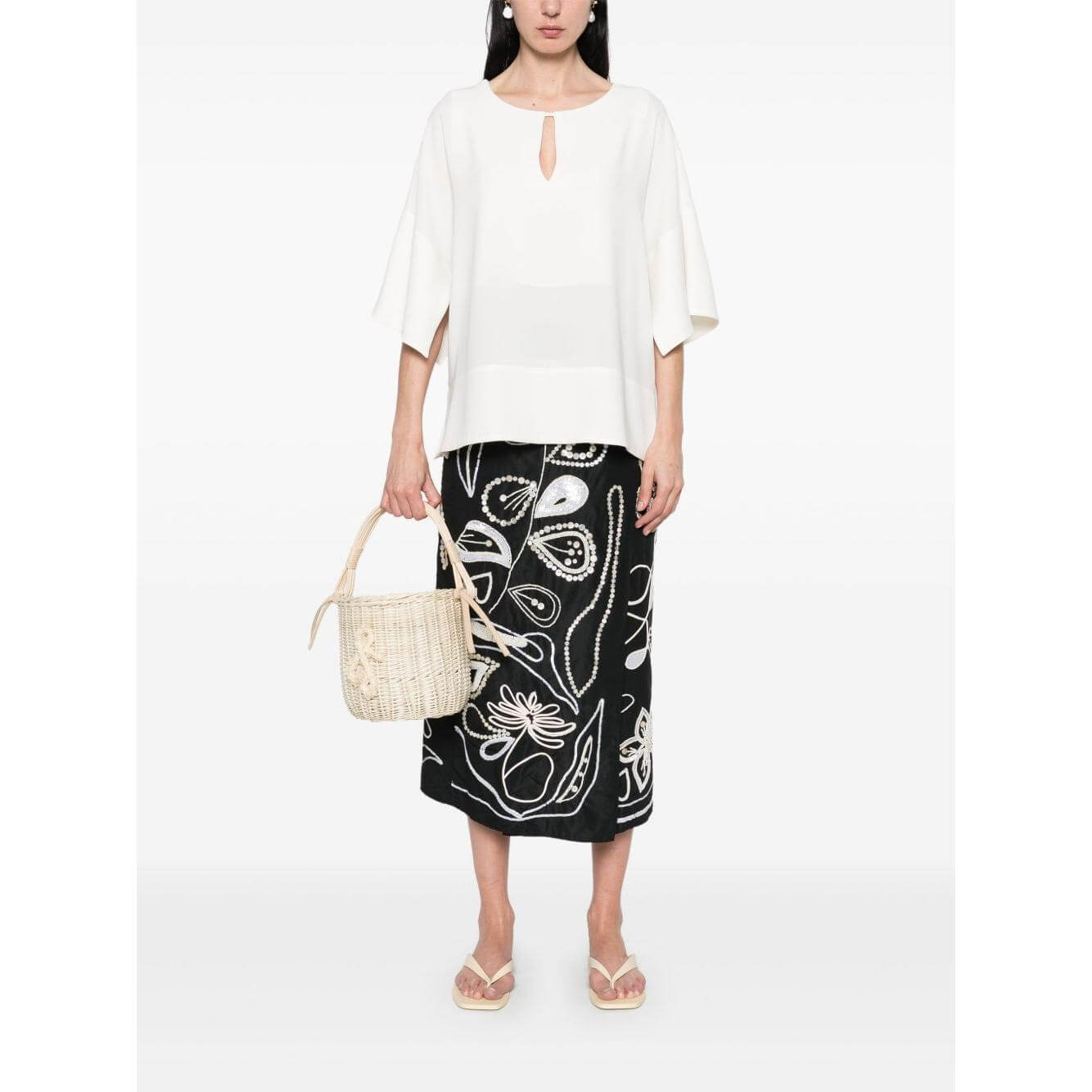 Model wearing Alberto Biani white teardrop opening blouse, three-quarter drop shoulder sleeves, paired with a patterned skirt and straw bag.