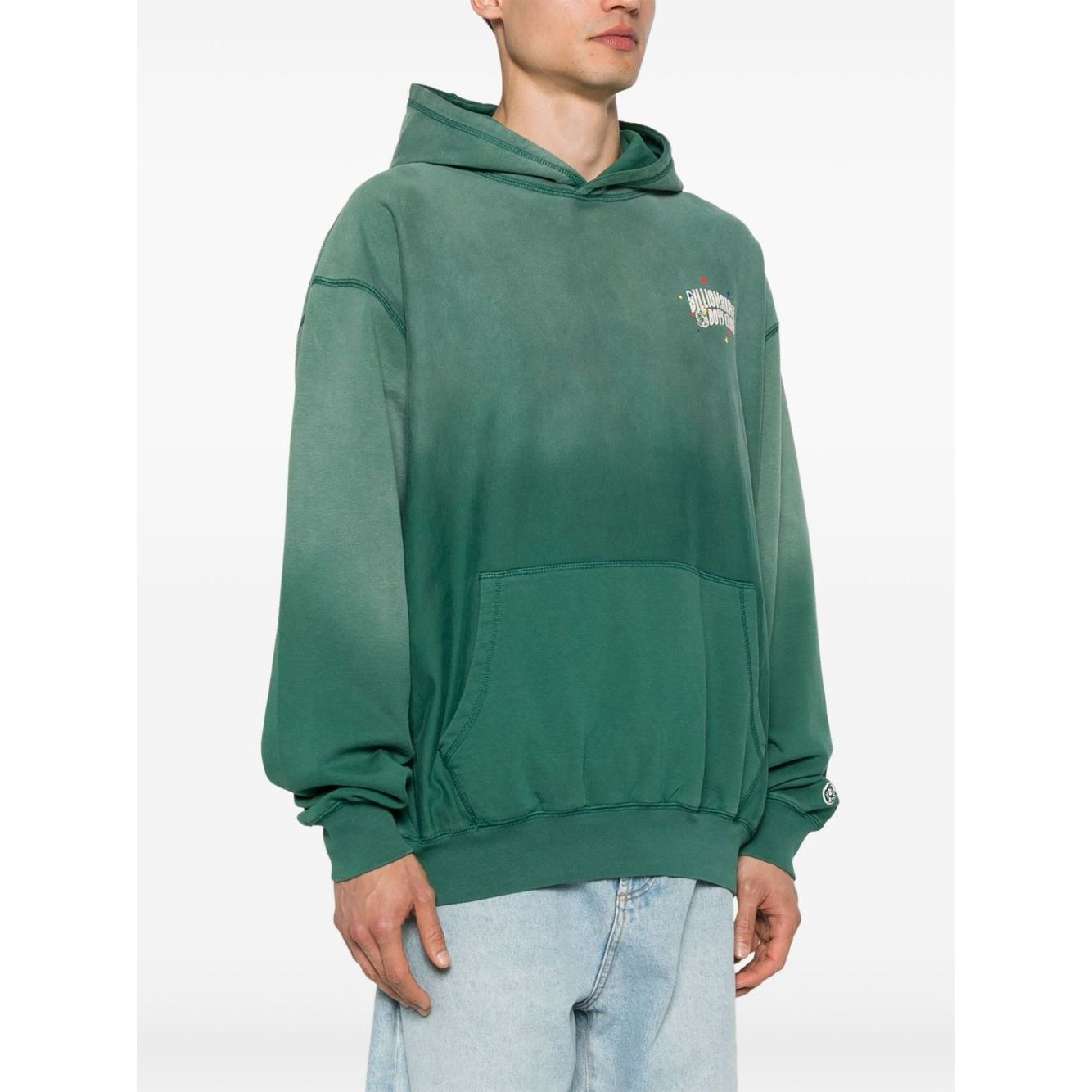 Model wearing Billionaire Sweaters Green hoodie with front pouch pocket, long sleeves, and logo patch on sleeve.