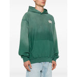 Model wearing Billionaire Sweaters Green hoodie with front pouch pocket, long sleeves, and logo patch on sleeve.