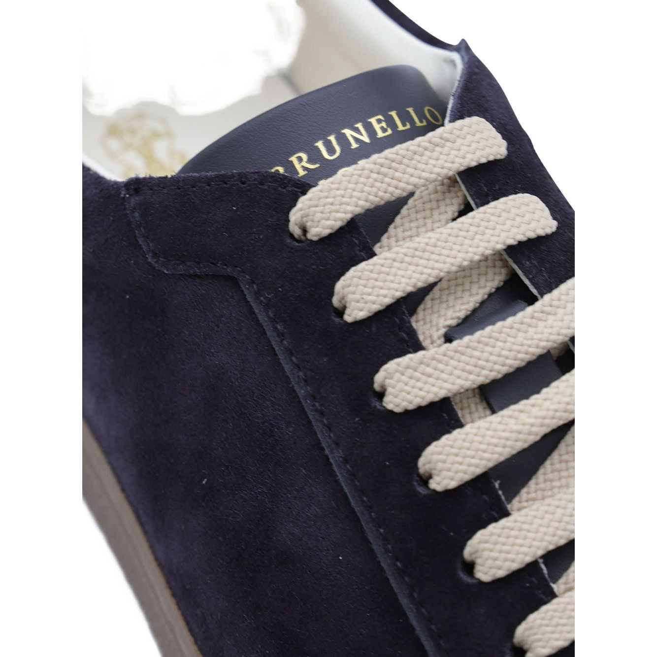 Close-up of Brunello Cucinelli Suede sneakers with dark blue suede upper and beige flat laces.