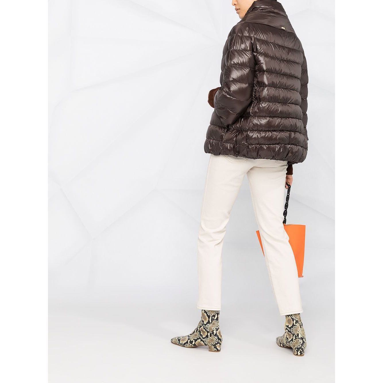 Woman wearing Herno Jackets Brown with padded design and high neck, paired with white pants and orange bag.