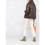 Woman wearing Herno Jackets Brown with padded design and high neck, paired with white pants and orange bag.