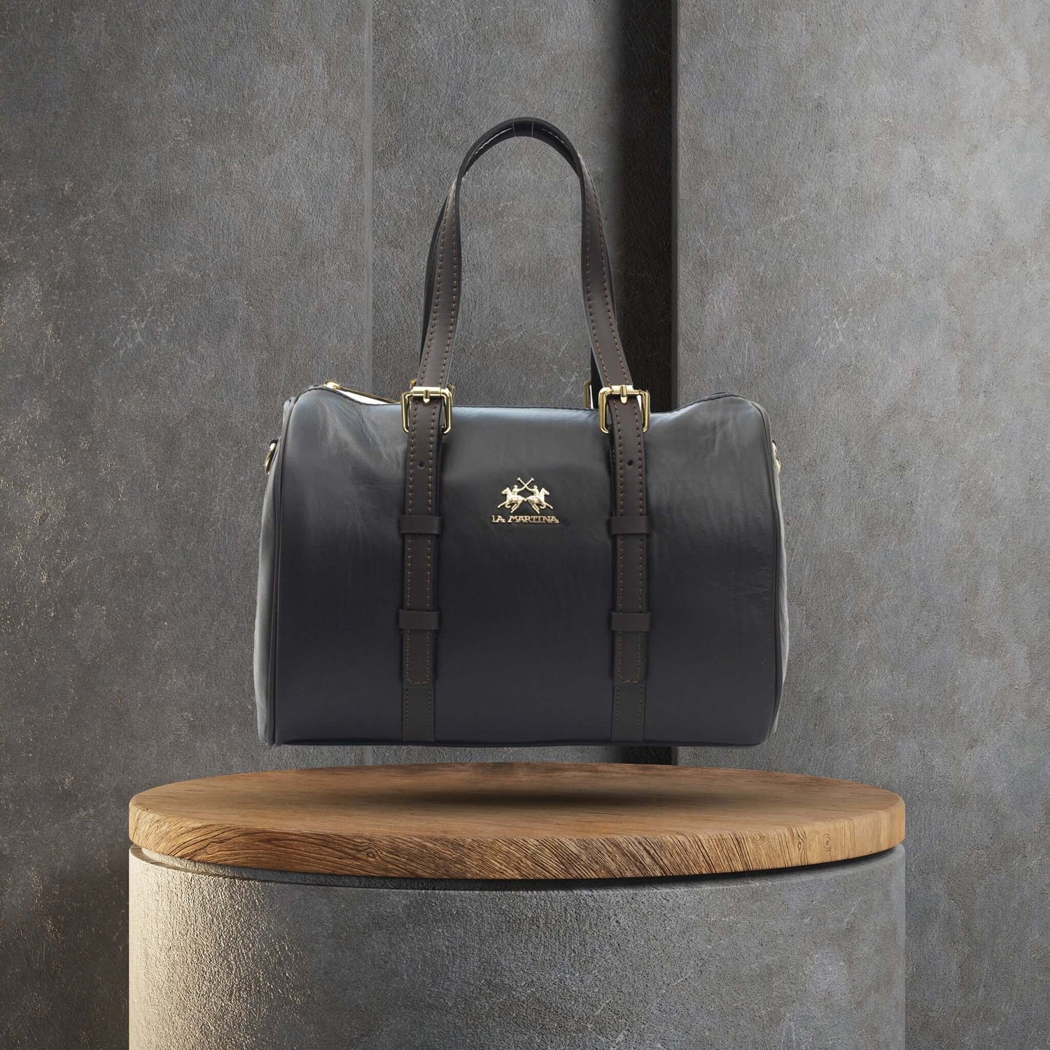 Luxury black leather handbag with gold accents displayed on a wooden pedestal against a grey background.