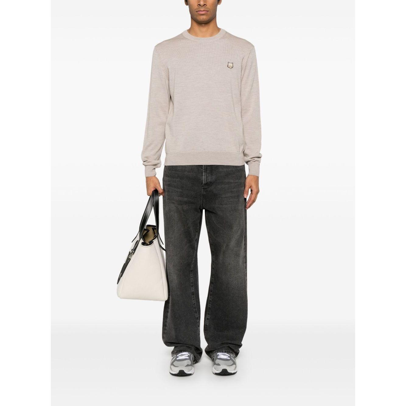 Man wearing Maison Kitsuné Maison Kitsune Fox motif sweater in light beige, with black jeans and sneakers, carrying a white bag.