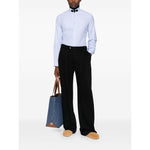 Model wearing Valentino Striped shirt in light blue with embroidered motif, styled with black trousers and carrying a blue tote bag.